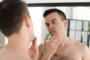 Handsome man after shaving looking at mirror in bathroom