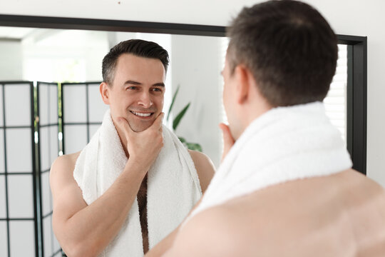 Smiling man after shaving looking at mirror in bathroom