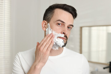 Handsome man applying shaving foam in bathroom