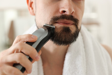 Man shaving with trimmer at home, closeup