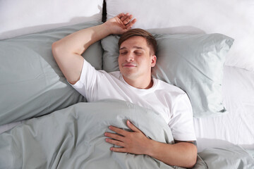Young man sleeping on bed with soft mattress at home, top view