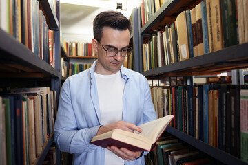 Man reading book near shelves in public library