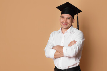 Happy student with crossed arms after graduation on beige background. Space for text