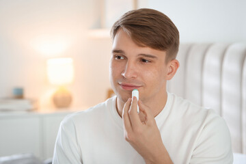 Young man applying lip balm onto his lips at home