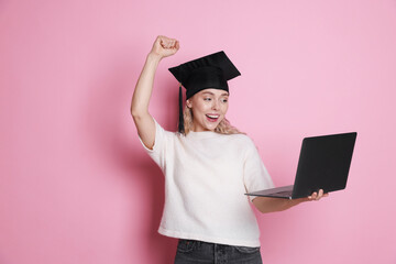 Happy student with laptop after graduation on pink background