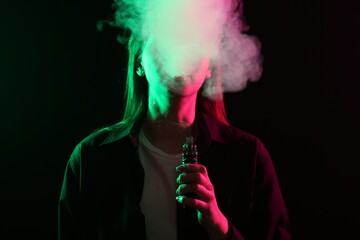 Woman using electronic smoking device in neon lights on black background