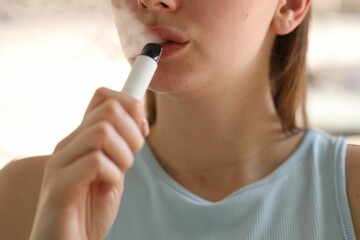Young woman using electronic smoking device outdoors, closeup