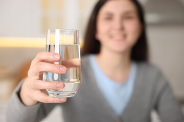 Woman with glass of water in kitchen, selective focus