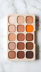 Fototapeta premium Neutral and warm toned eyeshadow palette with a vibrant orange shade on a marble background