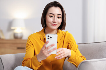 Woman using modern smartphone in armchair at home