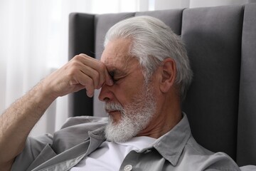 Senior man suffering from eyestrain on bed at home