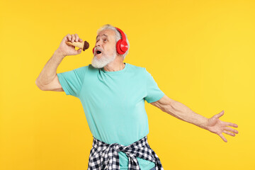 Elderly man in headphones with ice cream on orange background