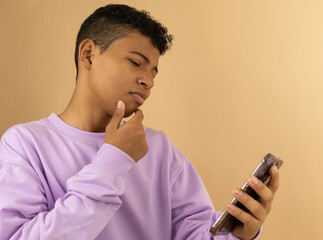 Brown skinned Latino teenager wearing a lilac sweatshirt thinking confusedly while looking at his...