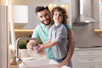Father and his son washing dishes together in kitchen at home