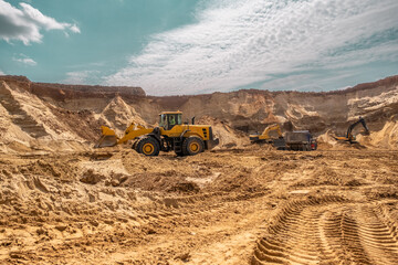 Close-up of tracks of a caterpillar tractor in the sand. In the distance, you can see equipment working in a sand quarry