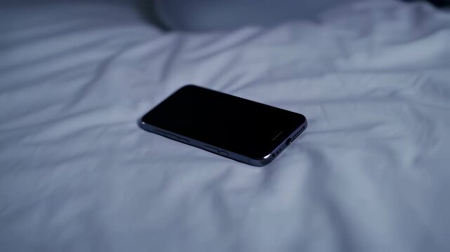 Hand reaching for smartphone on bed in dimly lit room demonstrating nighttime routine