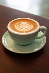 Cup of coffee with latte art on wooden table with soft sunlight.