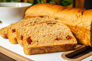 horizontal close-up photo of traditional artisan whole wheat sliced bread with guava jam next to a...