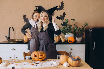 Mother and daughter smiling and preparing Halloween pumpkins in kitchen
