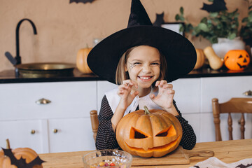 Little girl wearing witch costume posing with carved pumpkin for Halloween