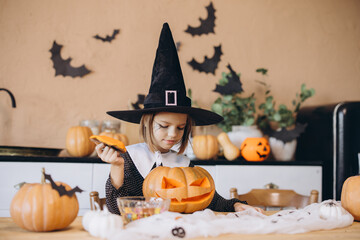 Little girl wearing witch costume carving pumpkin for Halloween party