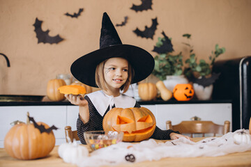 Little girl wearing witch costume carving Halloween pumpkin at home