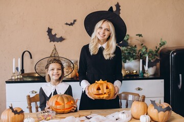Mother and daughter wearing witch costumes holding carved pumpkins for Halloween