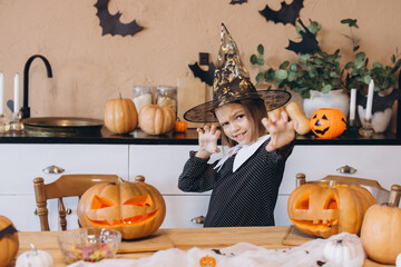 Little girl wearing witch costume posing with carved pumpkins for Halloween celebration
