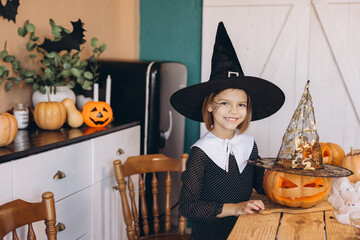 Smiling girl wearing witch costume celebrating Halloween with carved pumpkins