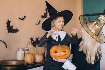 Mother and daughter wearing witch costumes preparing carved pumpkin for Halloween