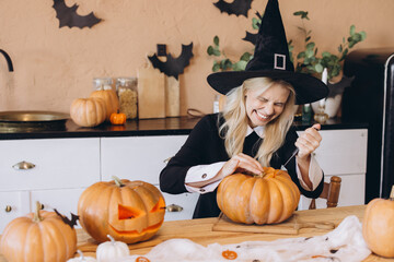 Woman wearing witch costume carving pumpkins for Halloween party at home