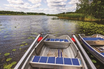 Fishing rental boats parked near pier on calm lake with lily pads under cloudy sky. Sweden.