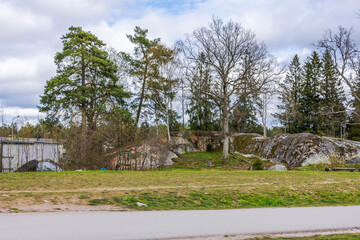 Large mossy rocks and spring trees in suburban area with forest background and sidewalk in foreground. Sweden.