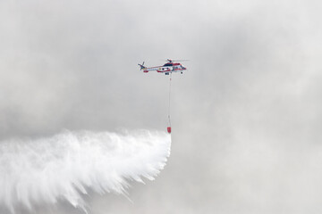 Firefighting helicopter releasing water in city sky