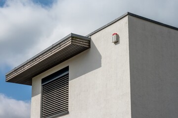 Modern house exterior showing security alarm and window with blinds on sunny day