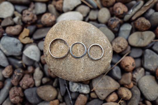Three wedding rings placed on a smooth stone surrounded by natural pebbles, symbolizing unity, love, and connection.
Three Wedding Rings on Stone Among Pebbles