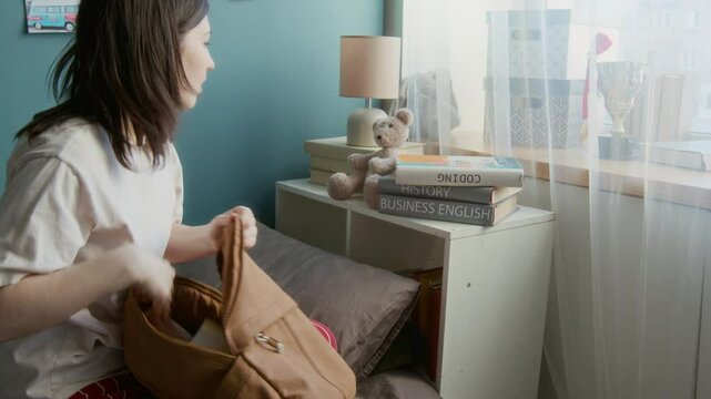 Side view medium shot of girl being late for classes and packing backpack rushing for school in dorm room