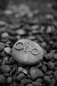 Three wedding rings placed on a smooth stone surrounded by natural pebbles, symbolizing unity, love, and connection.
Three Wedding Rings on Stone Among Pebbles