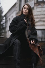 Young woman in stylish coat enjoys a quiet moment in a historic urban setting during a chilly...