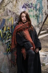 Woman in oversized coat and scarf poses against colorful graffiti in an abandoned urban setting...