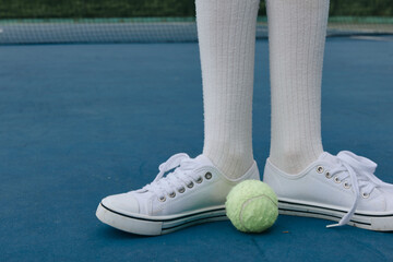 Young athlete standing on a tennis court with white sneakers and knee high socks, focused on the...
