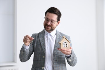 Real estate agent holding key with keychain and house model indoors