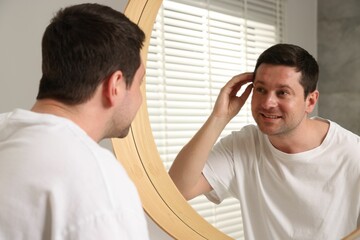 Obraz premium Handsome man looking at himself in mirror indoors