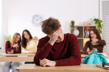 Bullying. Upset teenage boy and schoolmates pointing at him in classroom, selective focus