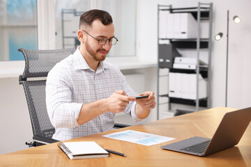 Man taking photo of document using scanning app on smartphone at desk in office