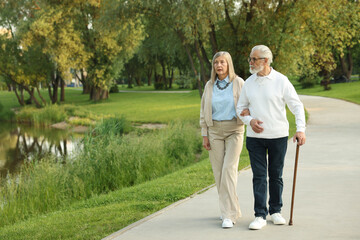 Fototapeta premium Lovely senior couple walking together near lake in park, space for text