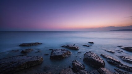 Obraz premium Captivating Twilight View of Rocky Shore With Calm Waves and Colorful Sky at Sunset by the Ocean