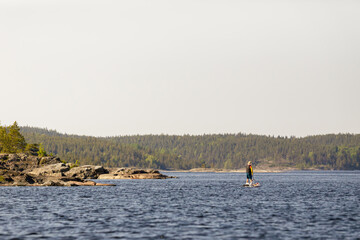 A person paddleboards across a tranquil lake with lush forests in the background, enjoying peaceful...
