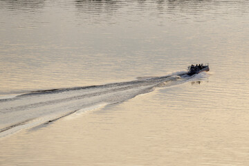 A boat leaves a trail of ripples on the smooth water surface, capturing the peaceful yet dynamic...