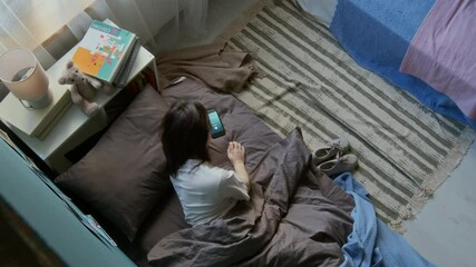 Top view shot of teenage girl waking up in morning and switching off loud smartphone alarm clock while lying in bed, copy space